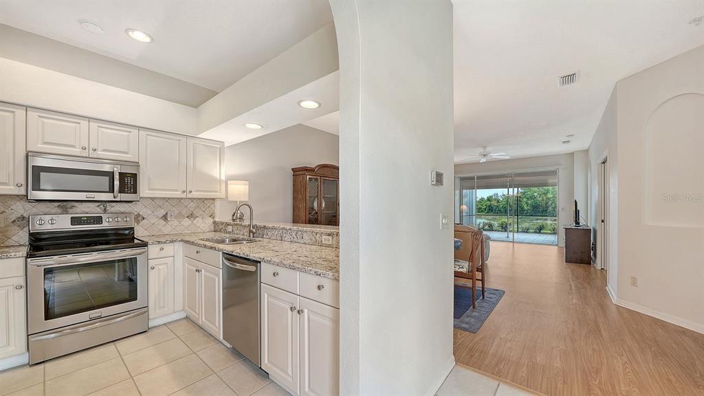 A kitchen with white cabinets and granite countertops opens to a living area with water views — 5126 BLUE ASH AVENUE, SARASOTA, FL