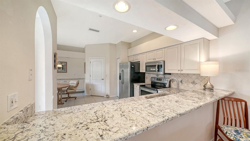 A kitchen with granite countertops, white cabinets, stainless steel appliances, and a breakfast bar — 5126 BLUE ASH AVENUE, SARASOTA, FL