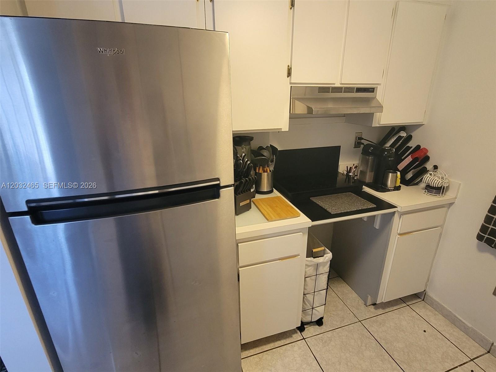 A small kitchen features white cabinets, a stainless steel refrigerator, and a black countertop — 2600 Collins Ave # 201, Miami Beach FL 33140, MIAMI BEACH, FL