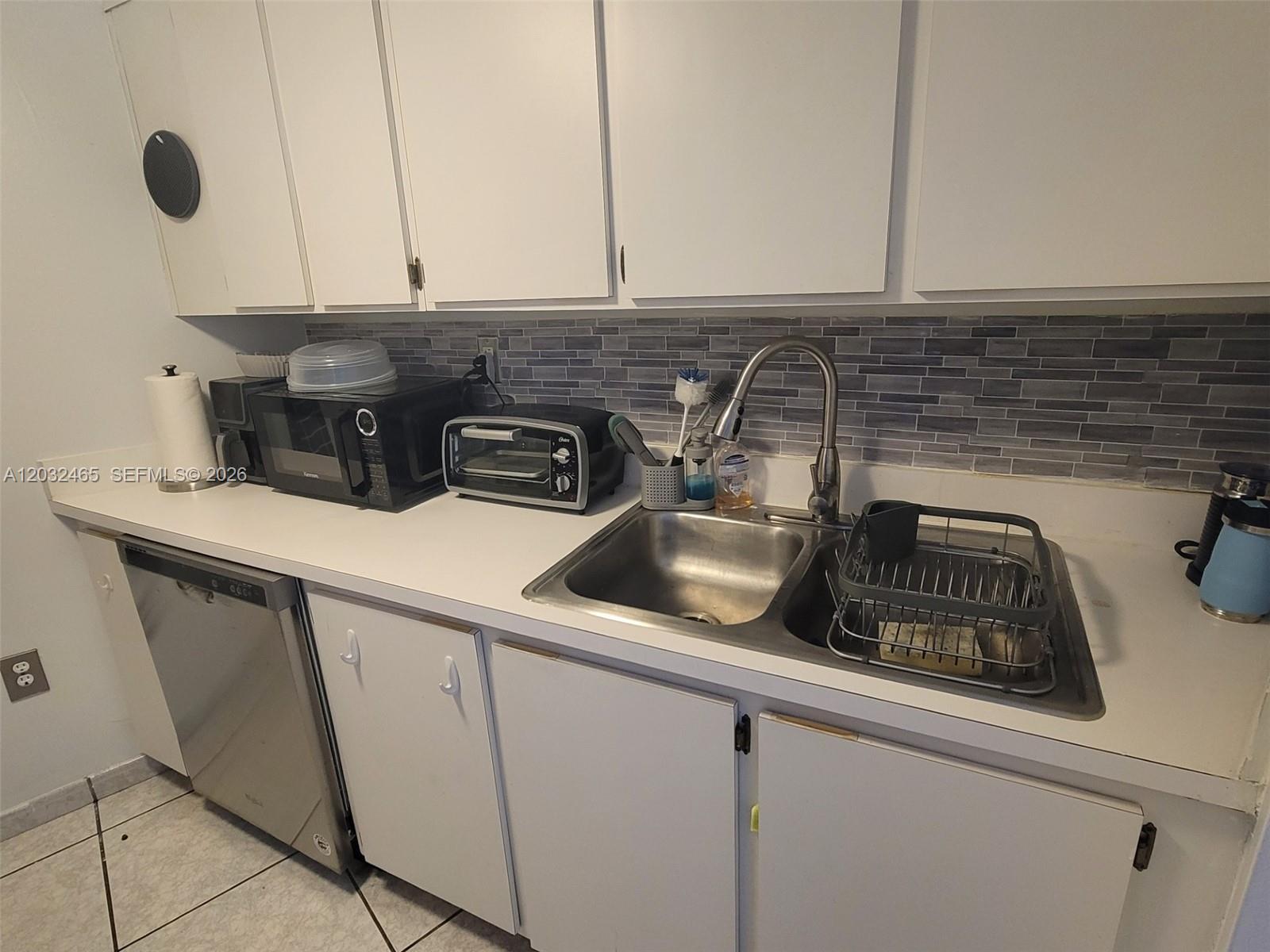 A kitchen features white cabinets, a stainless steel dishwasher, a double sink, and tiled backsplash — 2600 Collins Ave # 201, Miami Beach FL 33140, MIAMI BEACH, FL