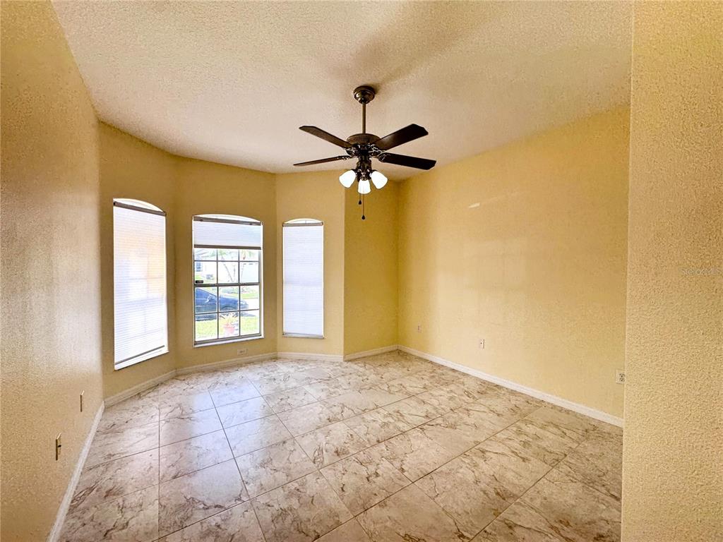 An empty room features yellow walls, tile flooring, a ceiling fan, and three bay windows — 140 MOSS LANE, DAVENPORT, FL