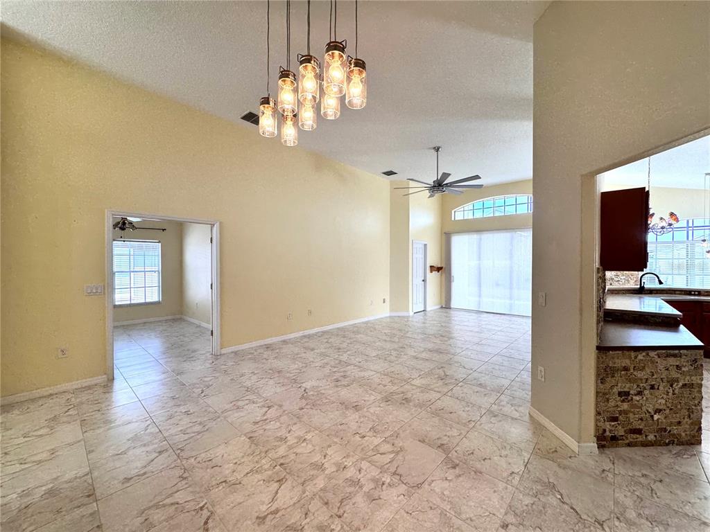 A spacious living area features tile flooring, a vaulted ceiling, and a multi-pendant light fixture — 140 MOSS LANE, DAVENPORT, FL
