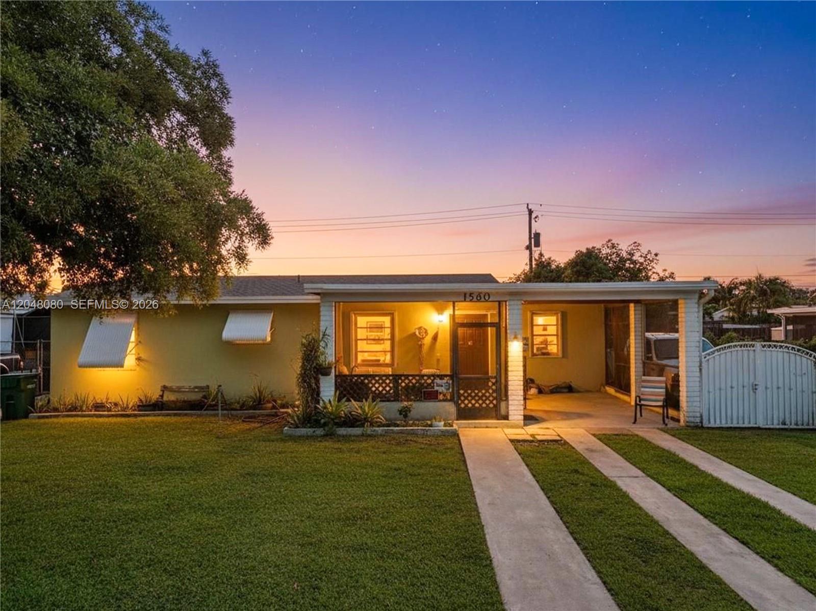 A single-story house with a lawn, a front porch, and a carport at dusk — 1560 NE 12th St, Homestead FL 33033, HOMESTEAD, FL