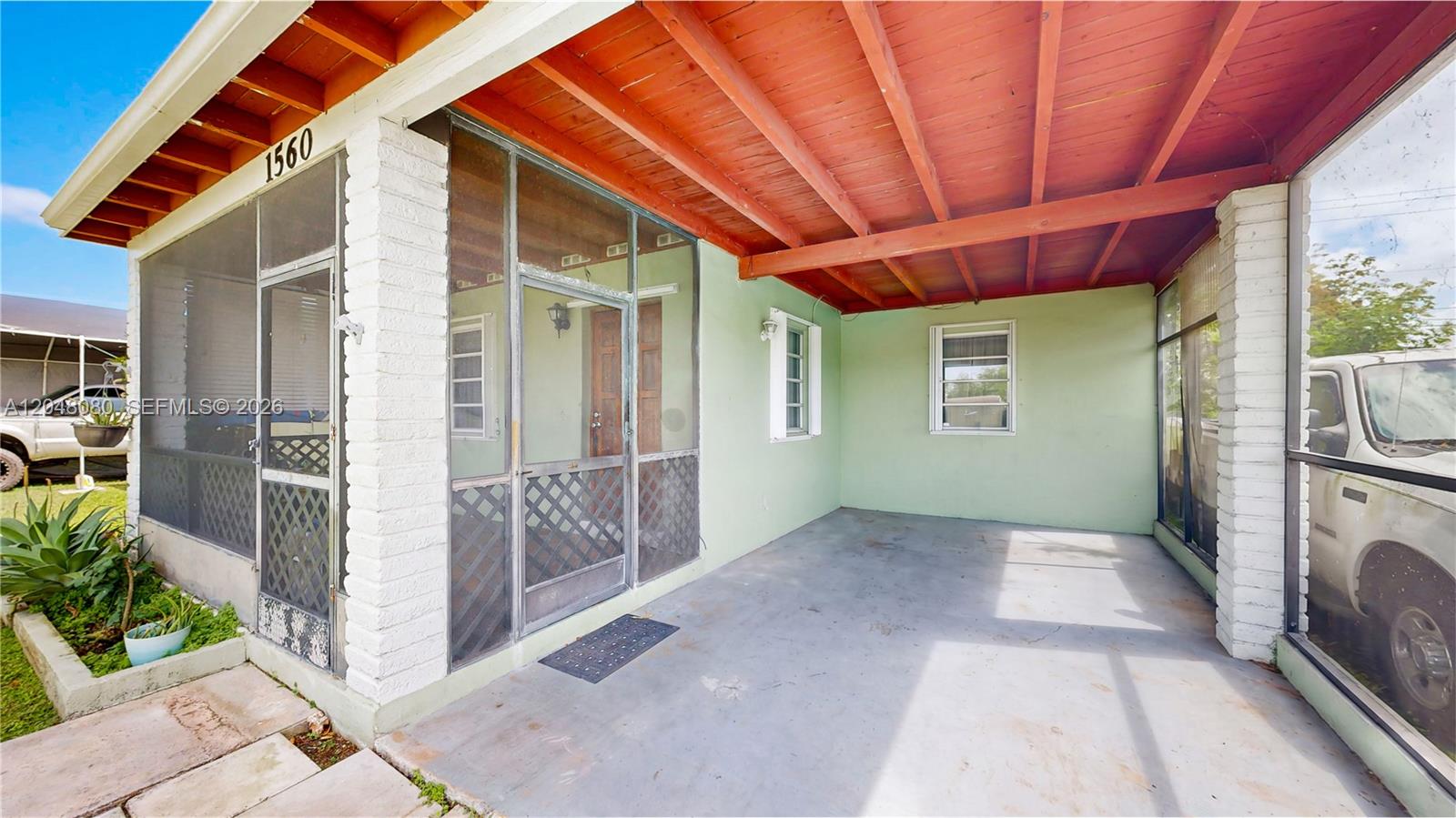A covered concrete patio features a screened-in entrance and an exposed wood beam ceiling — 1560 NE 12th St, Homestead FL 33033, HOMESTEAD, FL