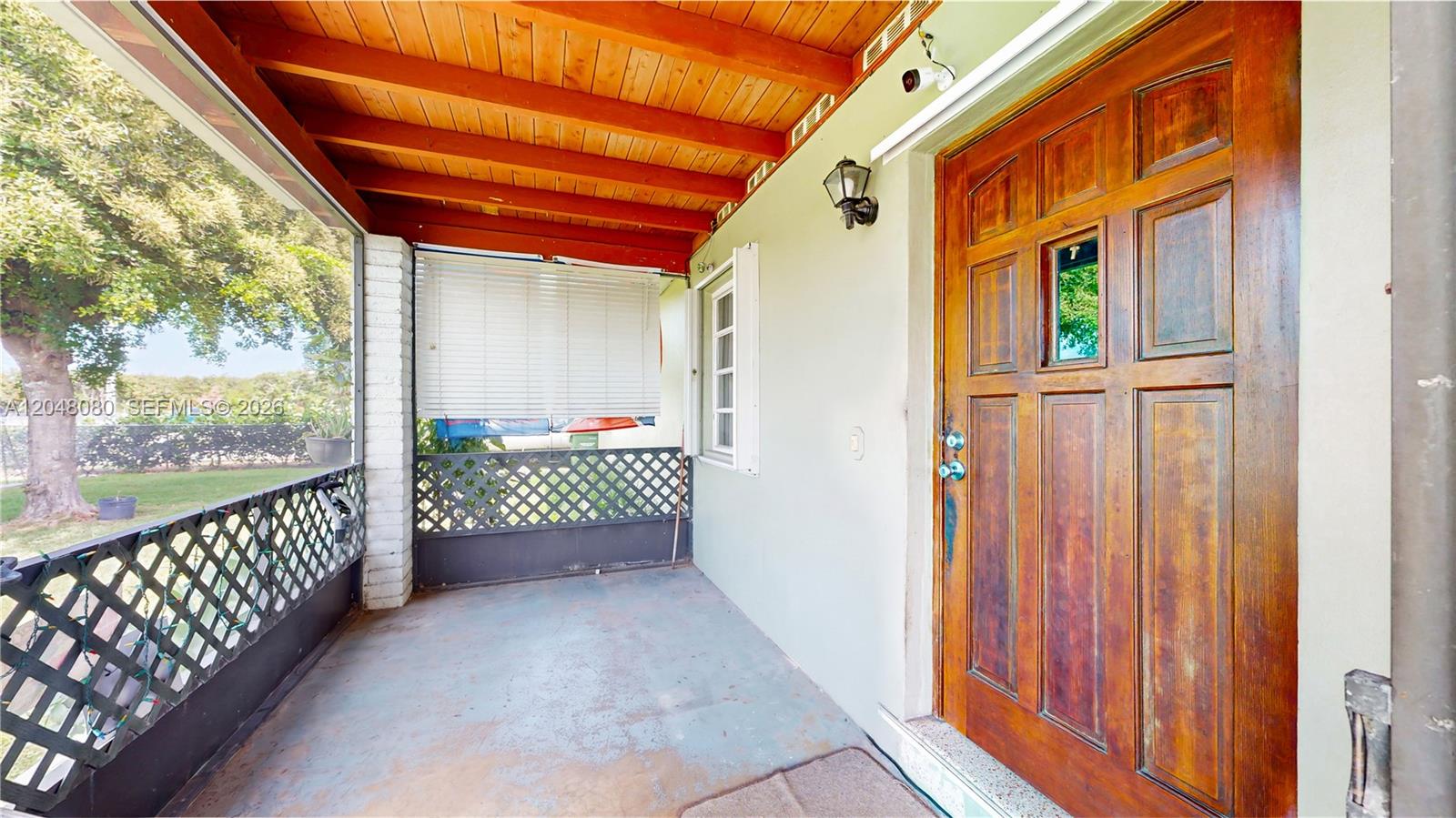 A covered porch features a wooden ceiling, a wooden front door, and lattice railings — 1560 NE 12th St, Homestead FL 33033, HOMESTEAD, FL
