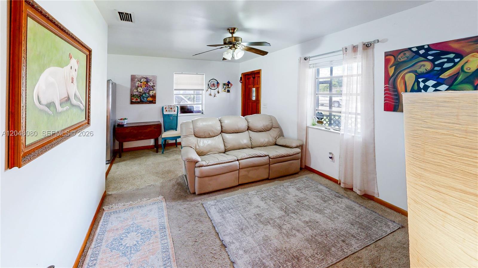 A living room features a beige reclining sofa, a ceiling fan, and two wall paintings — 1560 NE 12th St, Homestead FL 33033, HOMESTEAD, FL