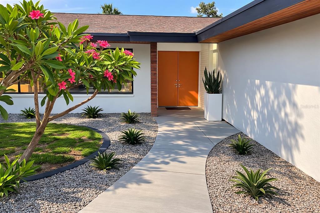 A modern home exterior features a bright orange double door, gravel landscaping, and a plumeria tree — 1901 UPPER COVE TERRACE, SARASOTA, FL