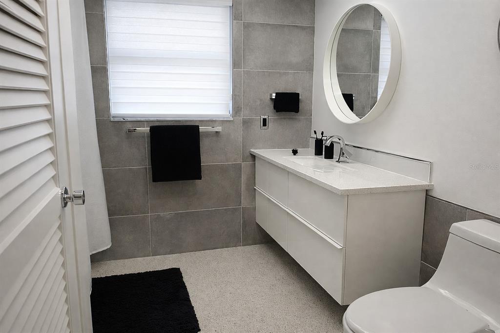 A modern bathroom features gray tiled walls, a white floating vanity, and a round mirror — 1901 UPPER COVE TERRACE, SARASOTA, FL