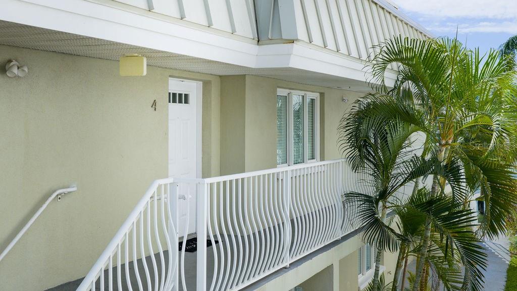 An exterior view of a building balcony featuring a white door labeled number four — 185 BRIGHTWATER DRIVE UNIT 4, CLEARWATER BEACH, FL