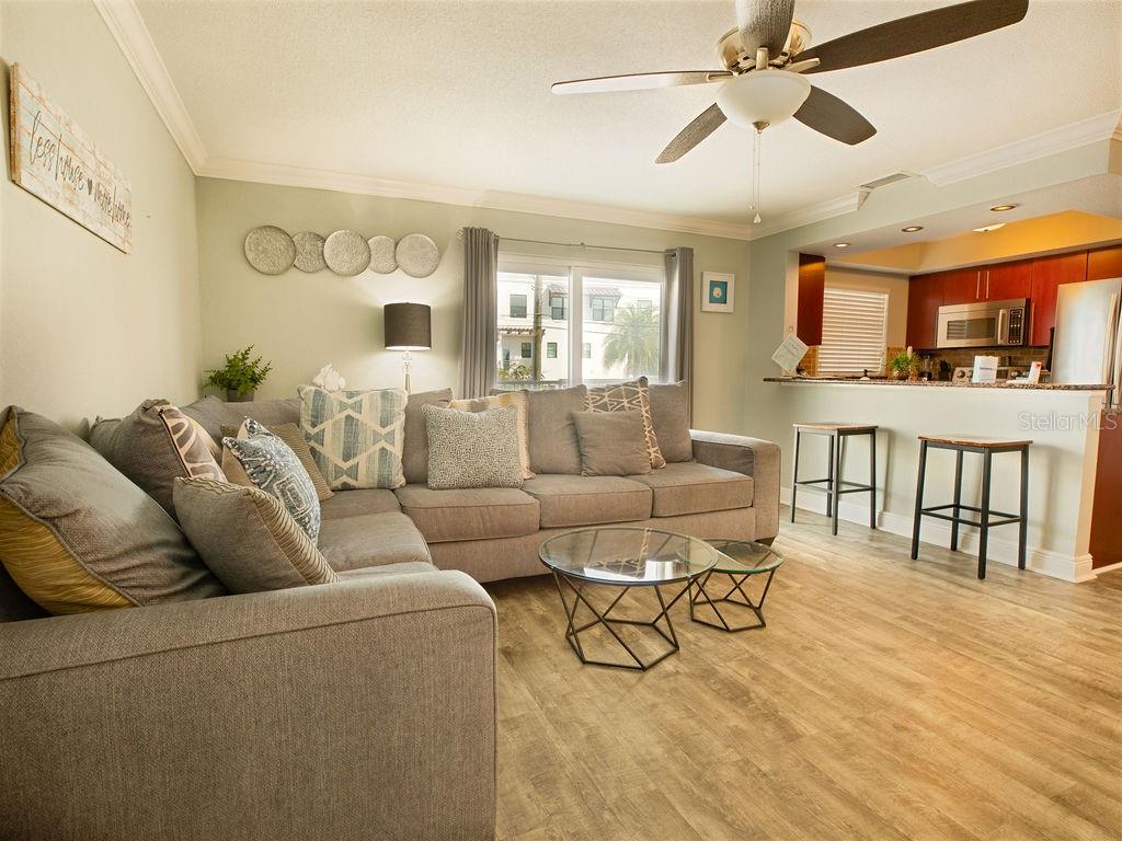 A living room with a gray sectional sofa, glass coffee tables, and an open kitchen — 185 BRIGHTWATER DRIVE UNIT 4, CLEARWATER BEACH, FL