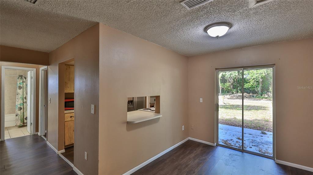 A dining area with wood-look flooring, a kitchen pass-through window, and sliding glass patio doors — 1802 N FERN PALM DRIVE, EDGEWATER, FL