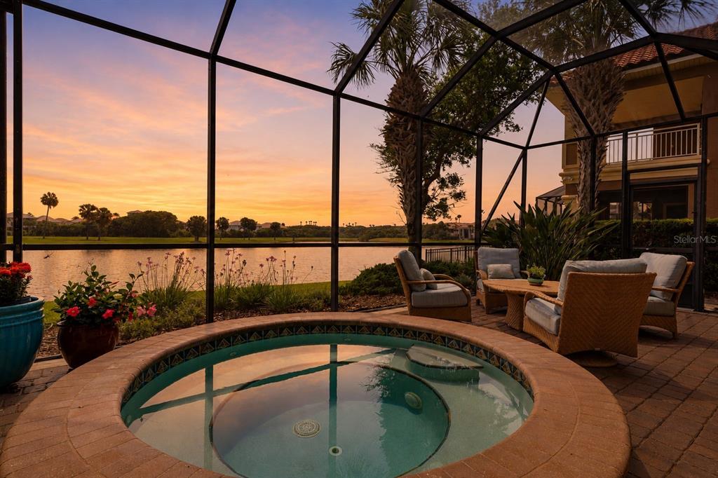 A screened-in patio features a circular hot tub, wicker furniture, and a lake sunset view — 34 KINGFISHER LANE, PALM COAST, FL