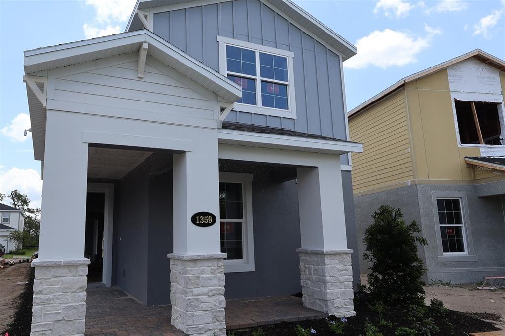 A two-story house exterior features a covered porch with stone pillars and gray siding — 1359 LUMPINI STREET, ST CLOUD, FL