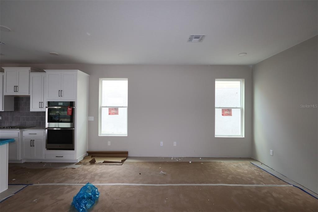 An unfinished kitchen and dining area features white cabinets, stainless steel appliances, and two windows — 1359 LUMPINI STREET, ST CLOUD, FL