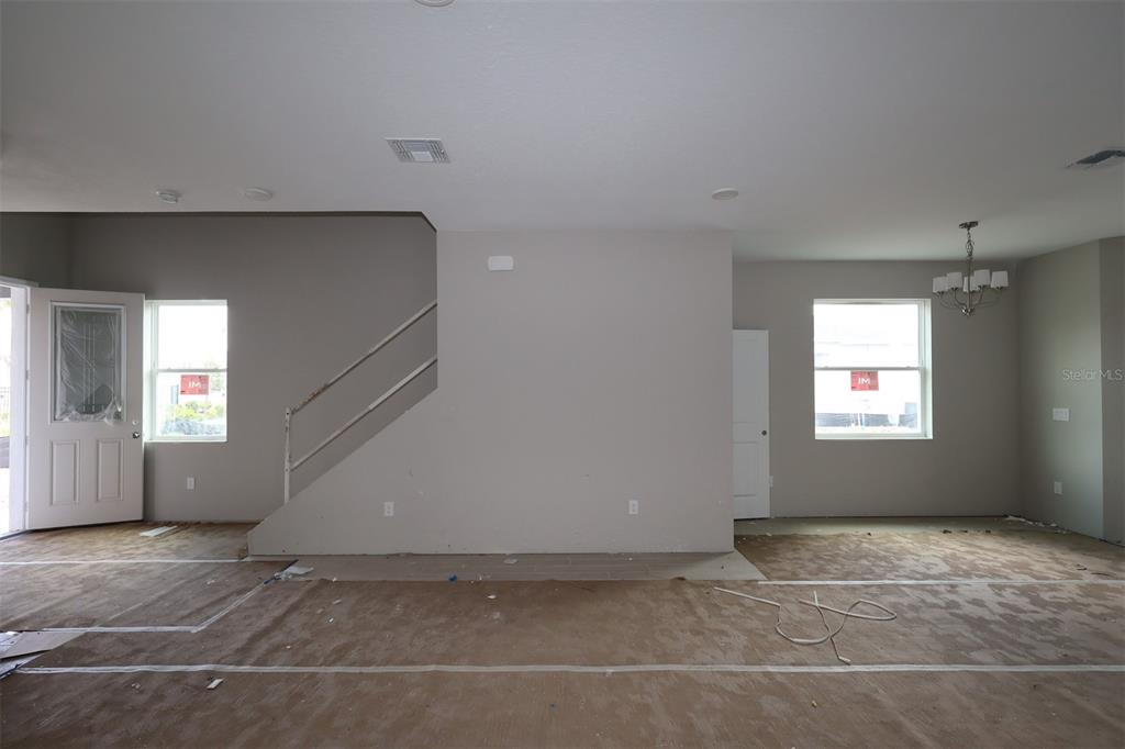 An unfinished room features a staircase, two windows, a chandelier, and protective floor covering — 1359 LUMPINI STREET, ST CLOUD, FL