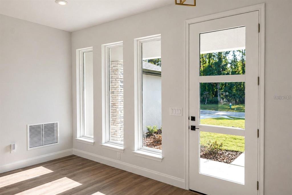 A bright room features wood-look flooring, three tall windows, and a white glass-paneled door — 14 POWDER HILL LANE, PALM COAST, FL