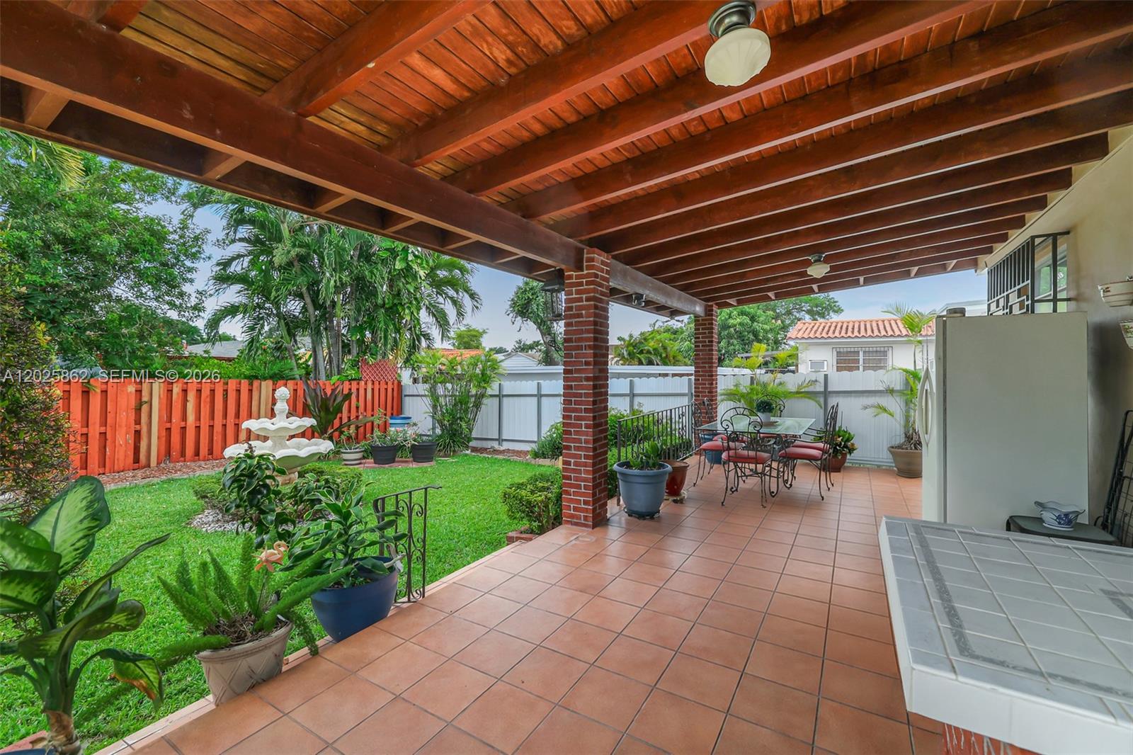 A covered patio with tiled flooring overlooks a backyard garden with a fountain — 251 NW 60th Ct, Miami FL 33126, MIAMI, FL