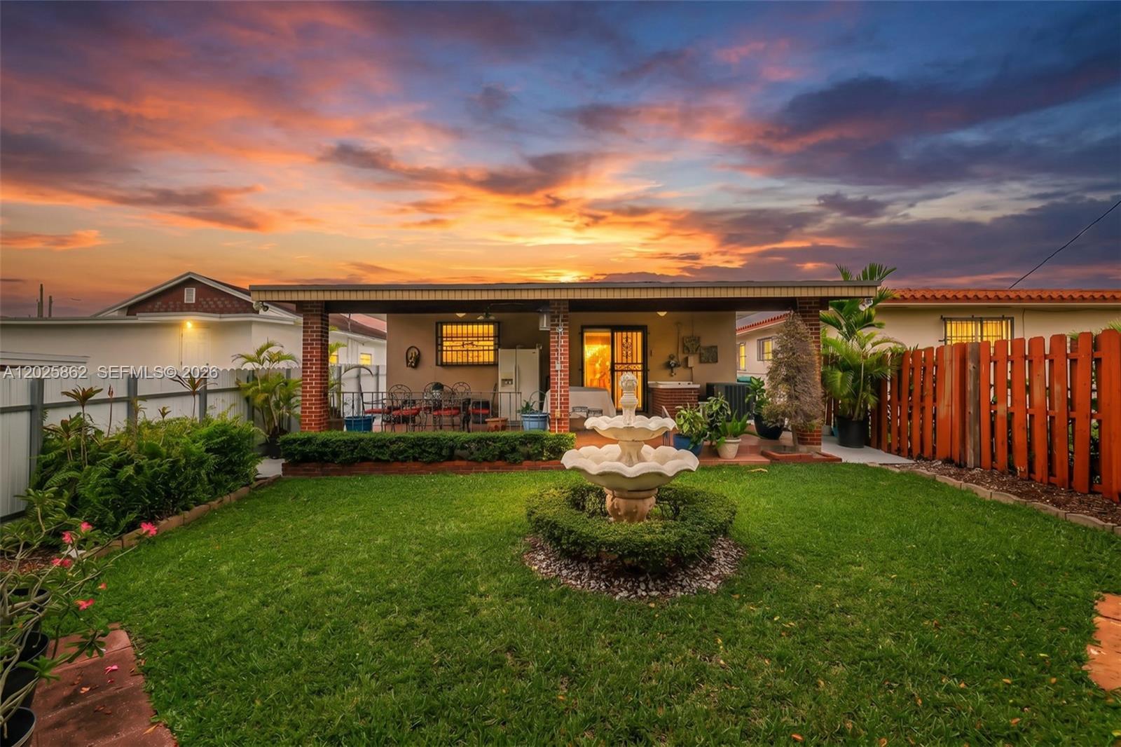 A backyard features a lawn, a tiered stone fountain, and a covered patio at sunset — 251 NW 60th Ct, Miami FL 33126, MIAMI, FL