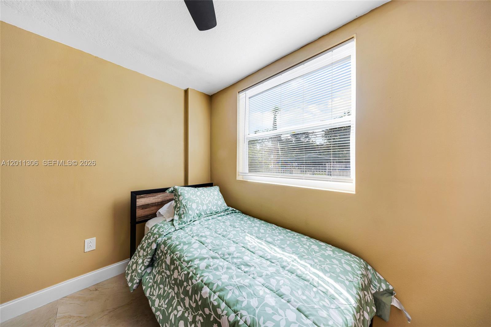 A bedroom features tan walls, a twin bed with a green patterned comforter, and blinds — 193 NW 58th St, Miami FL 33127, MIAMI, FL