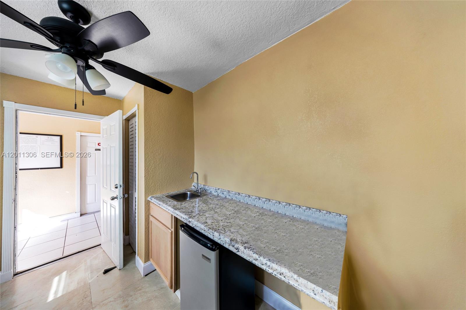 A small kitchenette features a granite countertop, a sink, and a mini-refrigerator against yellow walls — 193 NW 58th St, Miami FL 33127, MIAMI, FL