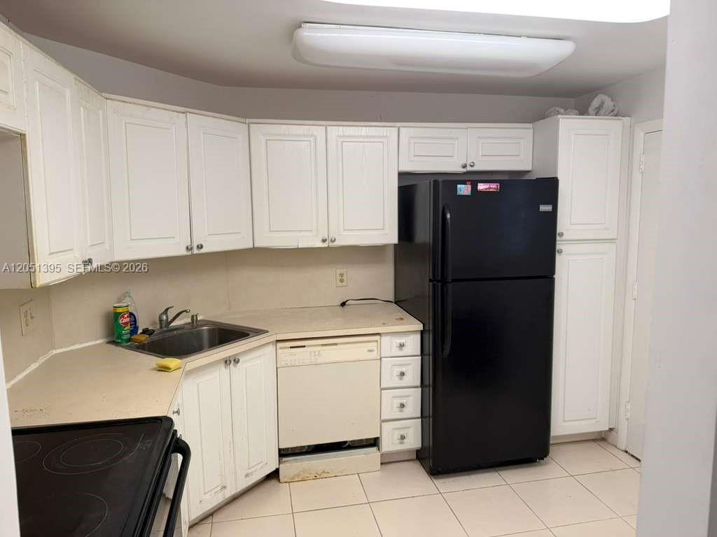 A kitchen features white cabinets, a black refrigerator, a stainless steel sink, and tile flooring — 3280 Spanish Moss Ter # 110, Lauderhill FL 33319, LAUDERHILL, FL