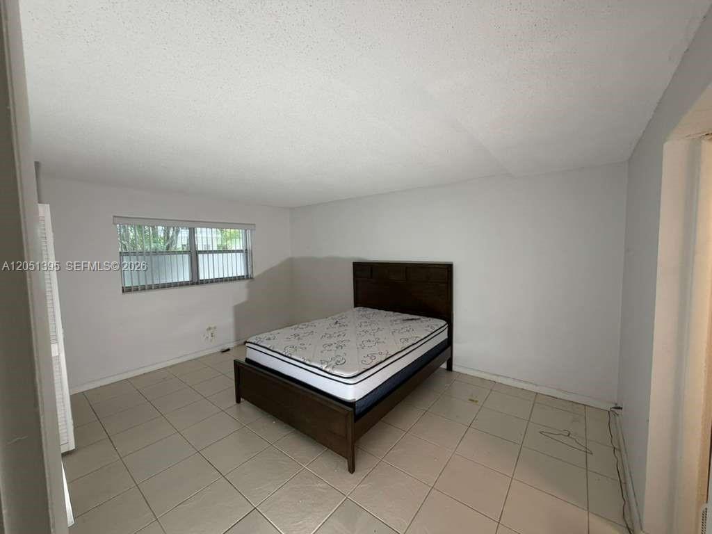 A bedroom features a dark wood bed frame, white walls, and light-colored tile flooring — 3280 Spanish Moss Ter # 110, Lauderhill FL 33319, LAUDERHILL, FL