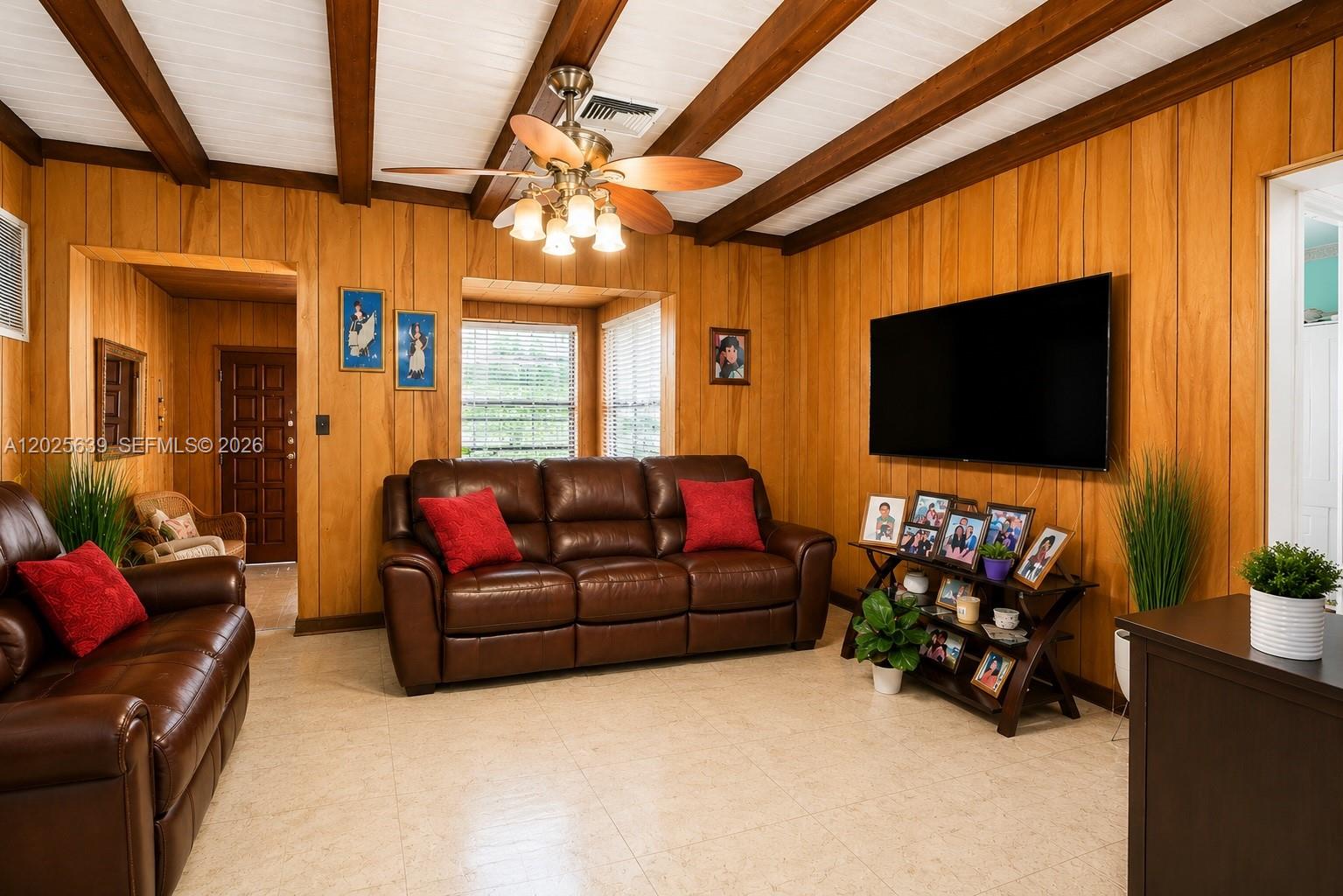 A living room features wood-paneled walls, exposed ceiling beams, a ceiling fan, and leather furniture — MIAMI, FL