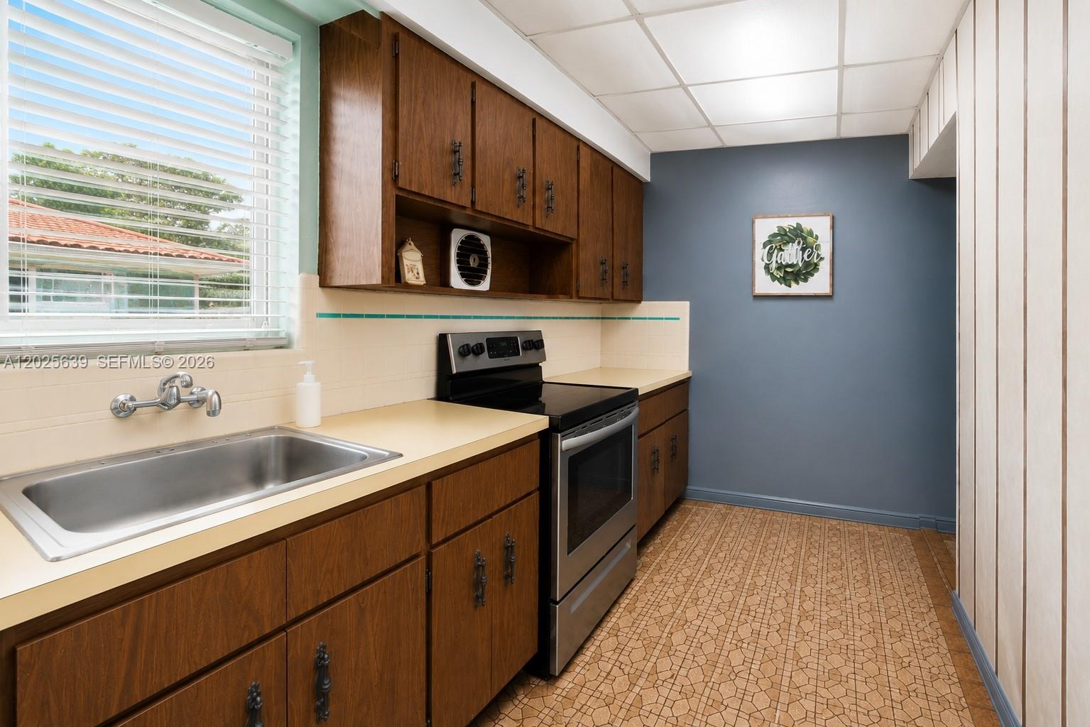 A kitchen features wood cabinets, a stainless steel stove, a sink, and patterned tile flooring — MIAMI, FL