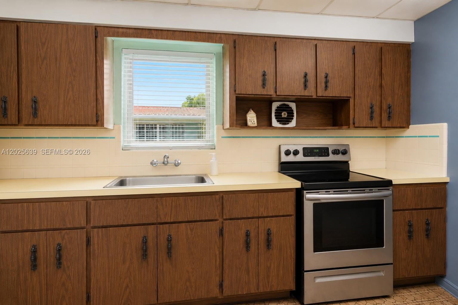 A kitchen features wood-grain cabinets, a stainless steel stove, and a window above the sink — MIAMI, FL