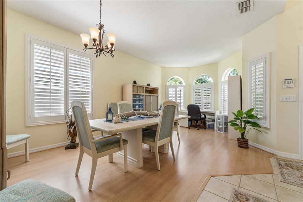A dining room with light wood floors, a central table, and large shuttered windows — 2248 HILLSHIRE DRIVE, ORLANDO, FL