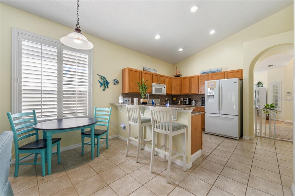 A kitchen with wood cabinets, a breakfast bar, and an adjacent dining area with shutters — 2248 HILLSHIRE DRIVE, ORLANDO, FL