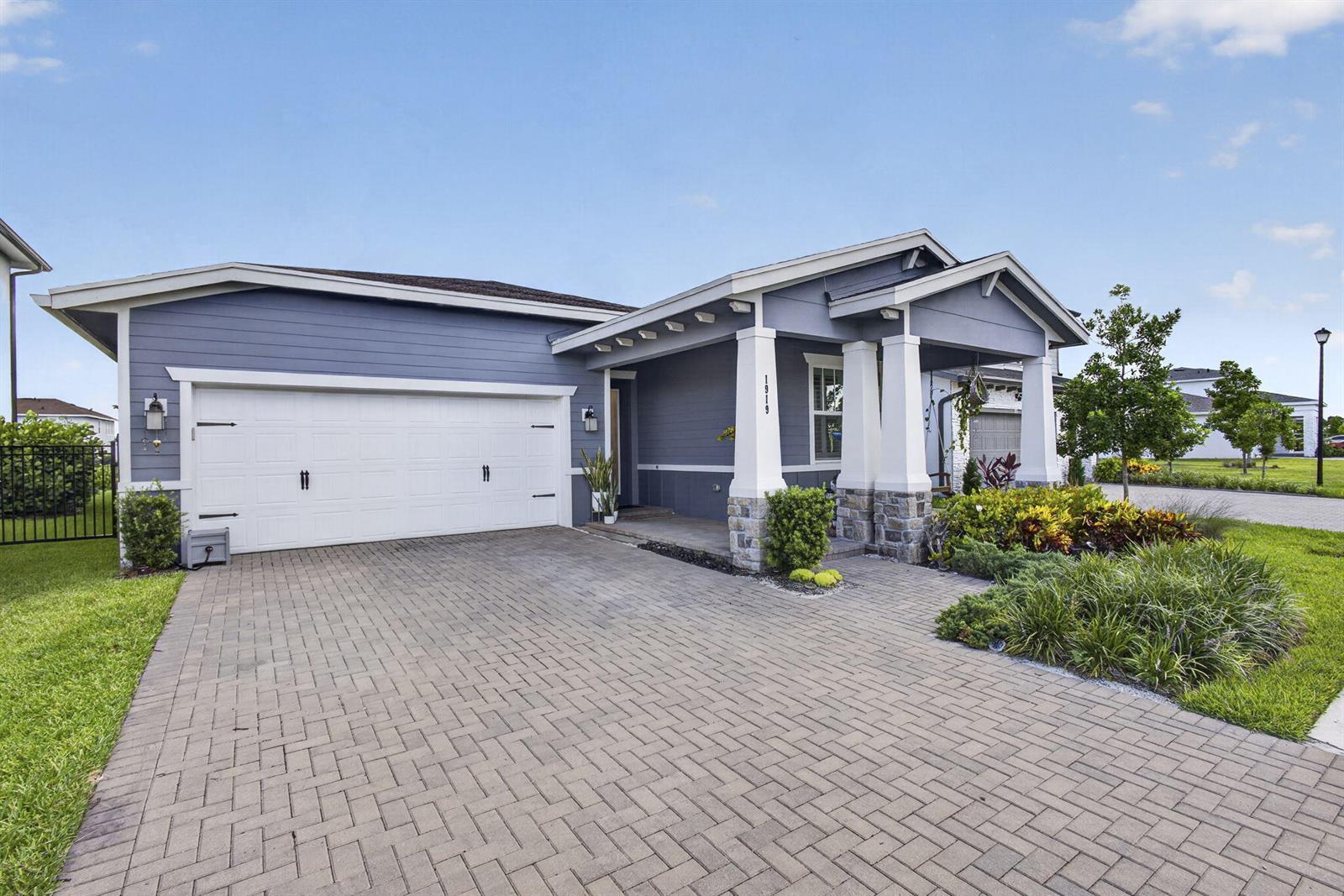 A blue house with a white garage door, stone-based columns, and a paved driveway — 1919 Wandering Willow Way, FL 33470, FL