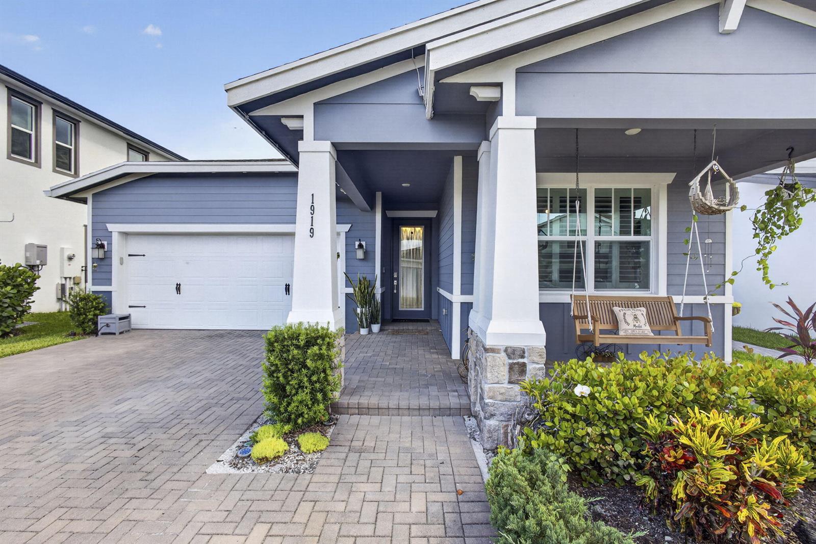 A blue house with a white-trimmed porch, stone pillars, and a paved driveway — 1919 Wandering Willow Way, FL 33470, FL