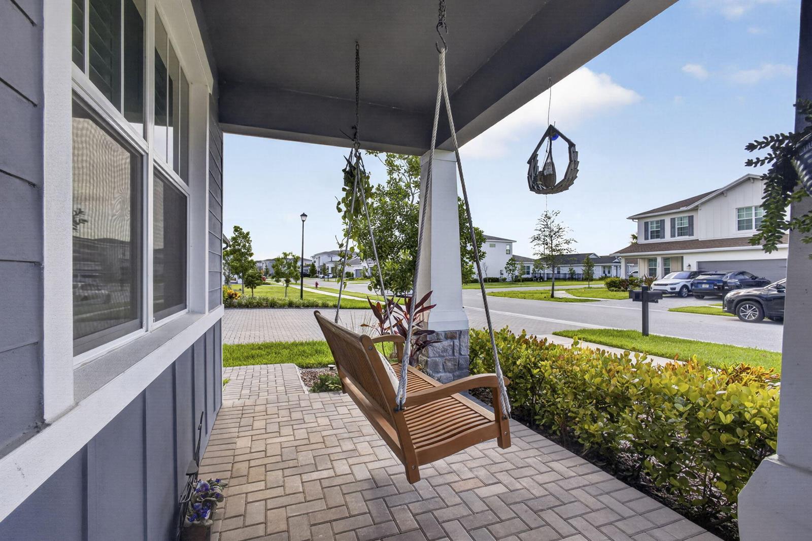 A wooden porch swing hangs on a paved front porch with a view of houses — 1919 Wandering Willow Way, FL 33470, FL