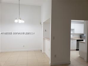 A dining area with a chandelier and tile floors leads into a white kitchen — 620 NE 12th Ave # 408, Hallandale Beach FL 33009, HALLANDALE BEACH, FL