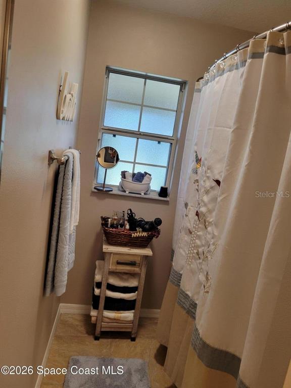A bathroom features a shower curtain, a window, and a small wooden storage stand — 1703 VALCOURT STREET NW, PALM BAY, FL