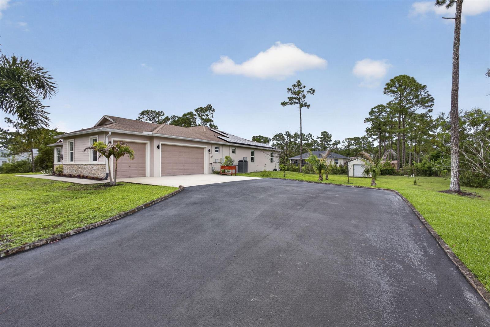 A tan house with a two-car garage and a large asphalt driveway sits on grass — 17145 Hamlin Boulevard, Loxahatchee FL 33470, LOXAHATCHEE, FL