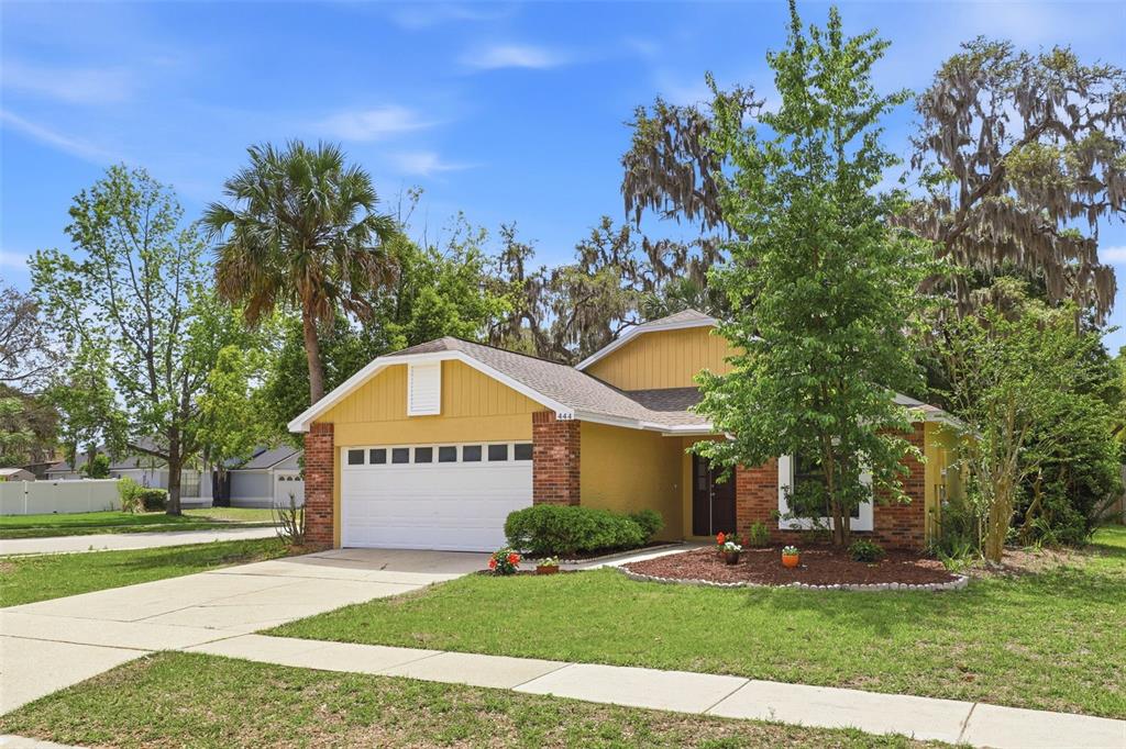 A yellow single-story house with a two-car garage, brick accents, and a front lawn — 444 MORNING GLORY DRIVE, LAKE MARY, FL