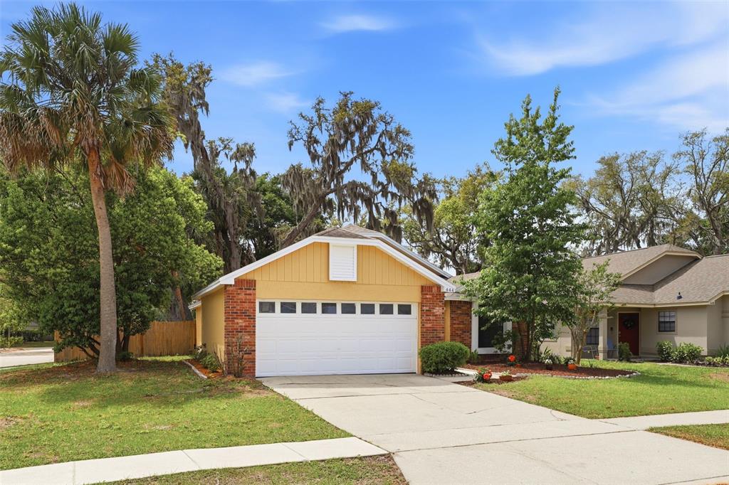 A yellow house with a brick-trimmed garage and a concrete driveway under a blue sky — 444 MORNING GLORY DRIVE, LAKE MARY, FL