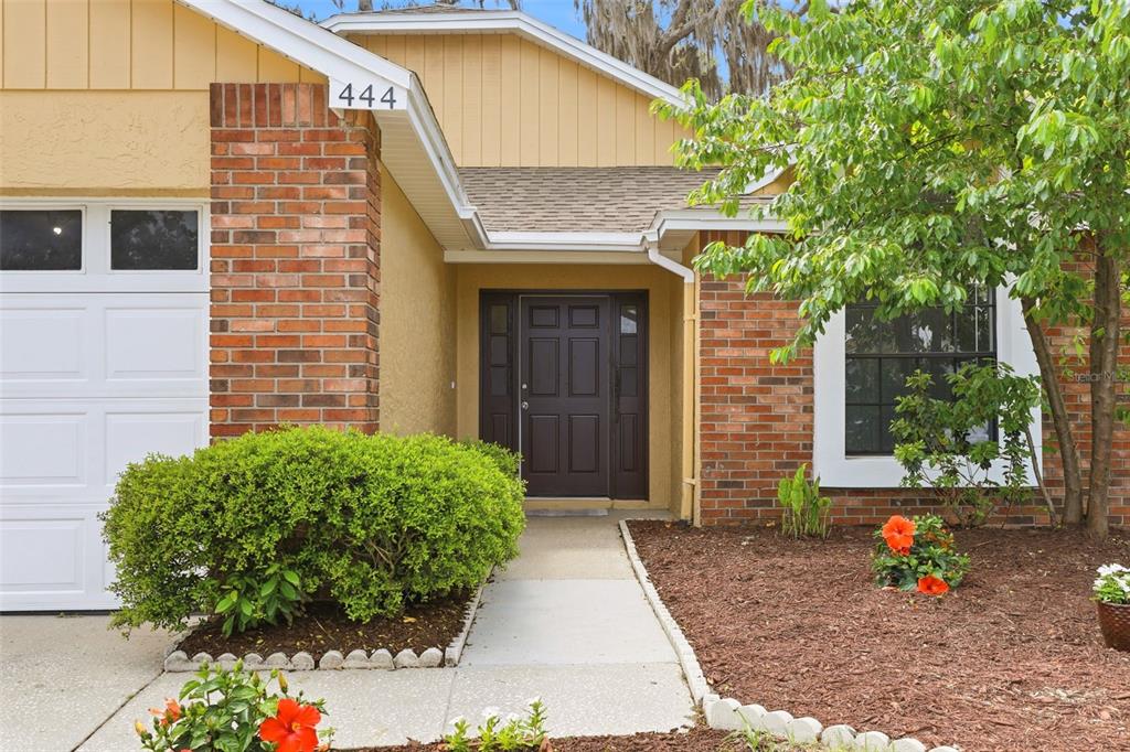 The exterior of a house features a brick facade, a dark front door, and landscaping — 444 MORNING GLORY DRIVE, LAKE MARY, FL