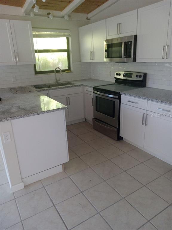 A kitchen features white cabinets, granite countertops, stainless steel appliances, and light-colored tile flooring — 1117 PATTERSON DRIVE UNIT Front, SARASOTA, FL