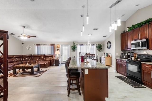 An open-concept living room and kitchen featuring dark wood cabinetry, granite countertops, and tile flooring — 1816 MANITOBA COURT, KISSIMMEE, FL