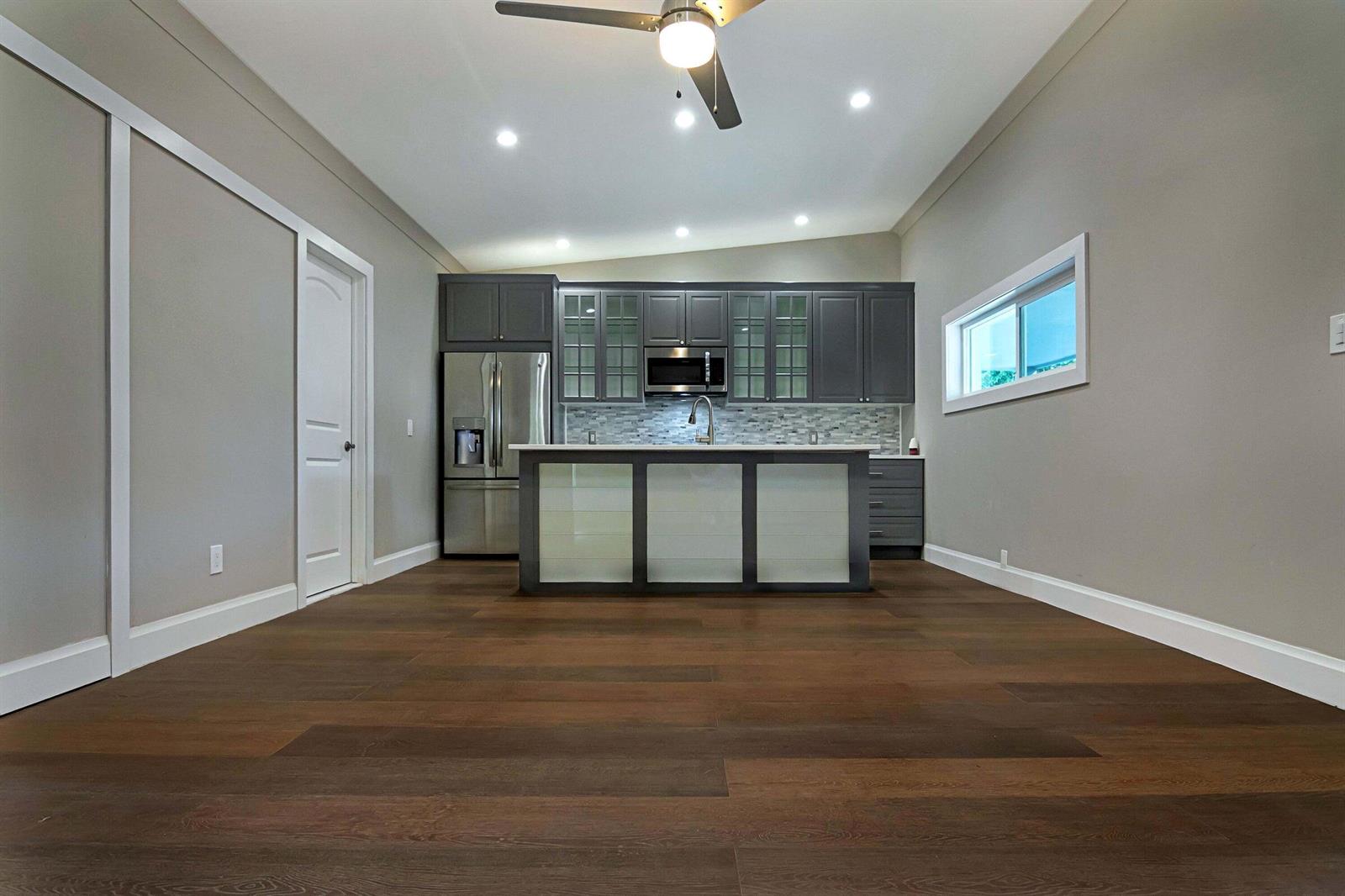 A modern kitchen features dark gray cabinetry, a central island, and dark wood-look flooring — 959 SW 18th Street, Boca Raton FL 33486, BOCA RATON, FL