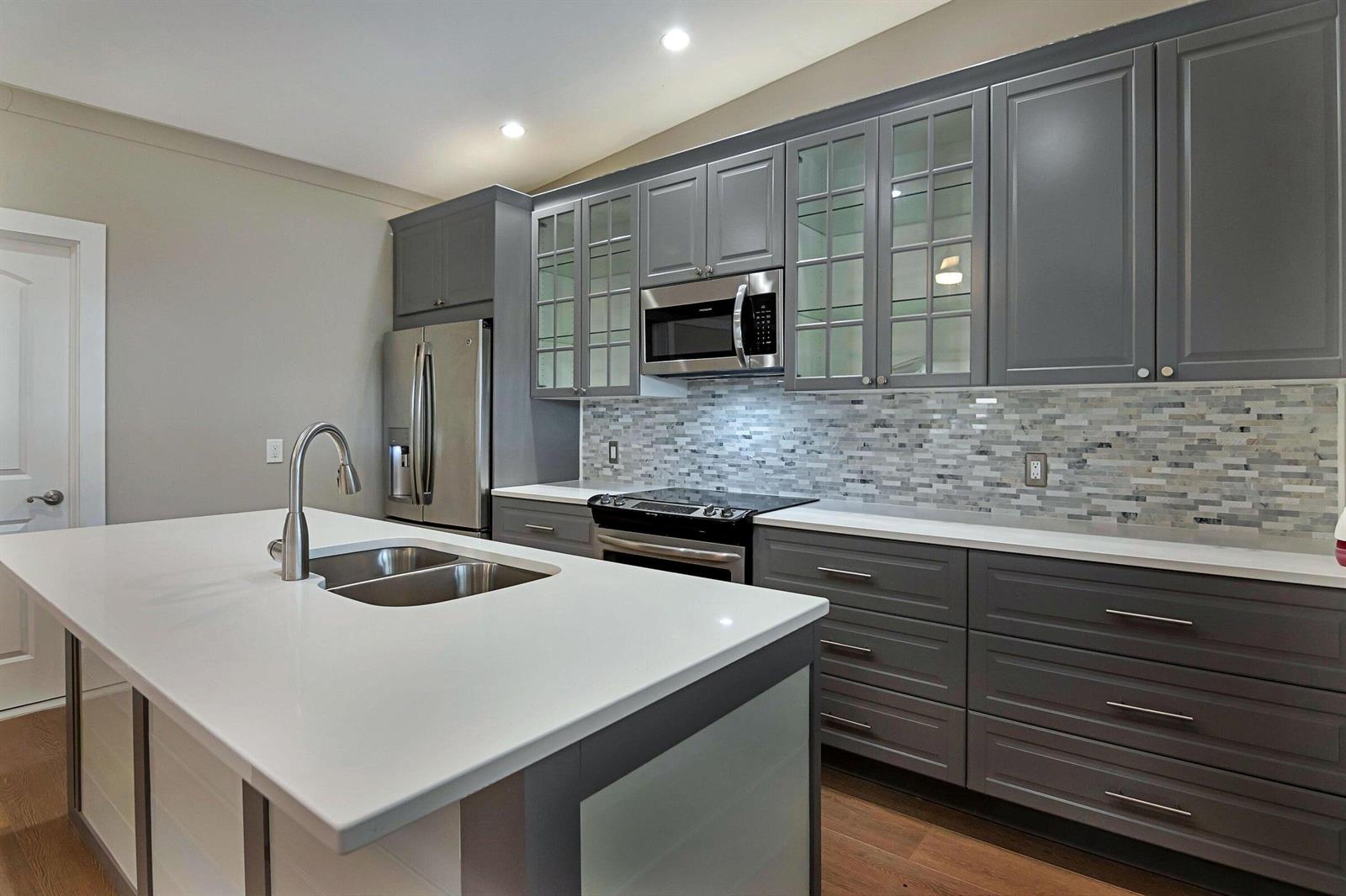 A modern kitchen features gray cabinets, a white quartz island countertop, and a tiled backsplash — 959 SW 18th Street, Boca Raton FL 33486, BOCA RATON, FL