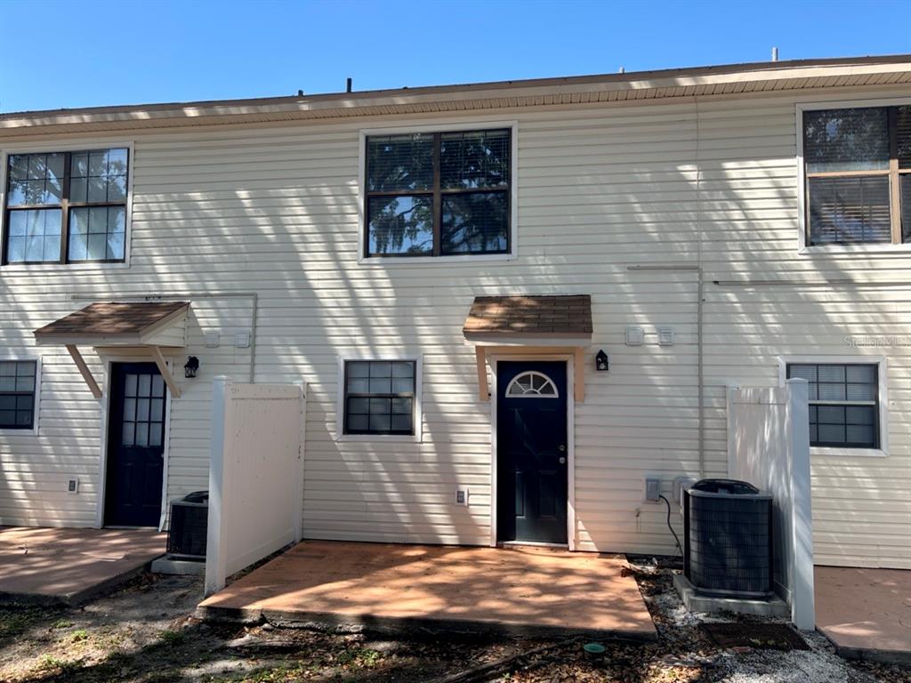 The exterior of a two-story townhouse features beige siding, two dark doors, and concrete patios — 2302 MAKI ROAD UNIT 25, PLANT CITY, FL