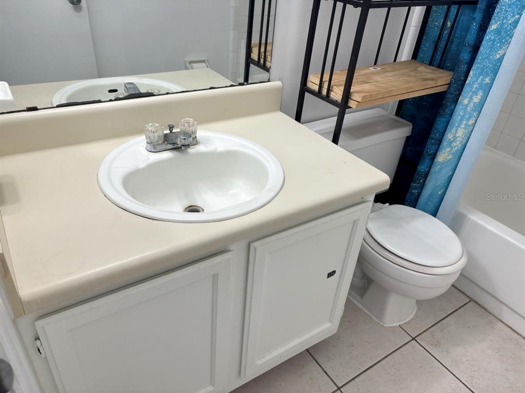 A bathroom features a white vanity with a beige countertop, a toilet, and metal shelving — 2302 MAKI ROAD UNIT 25, PLANT CITY, FL