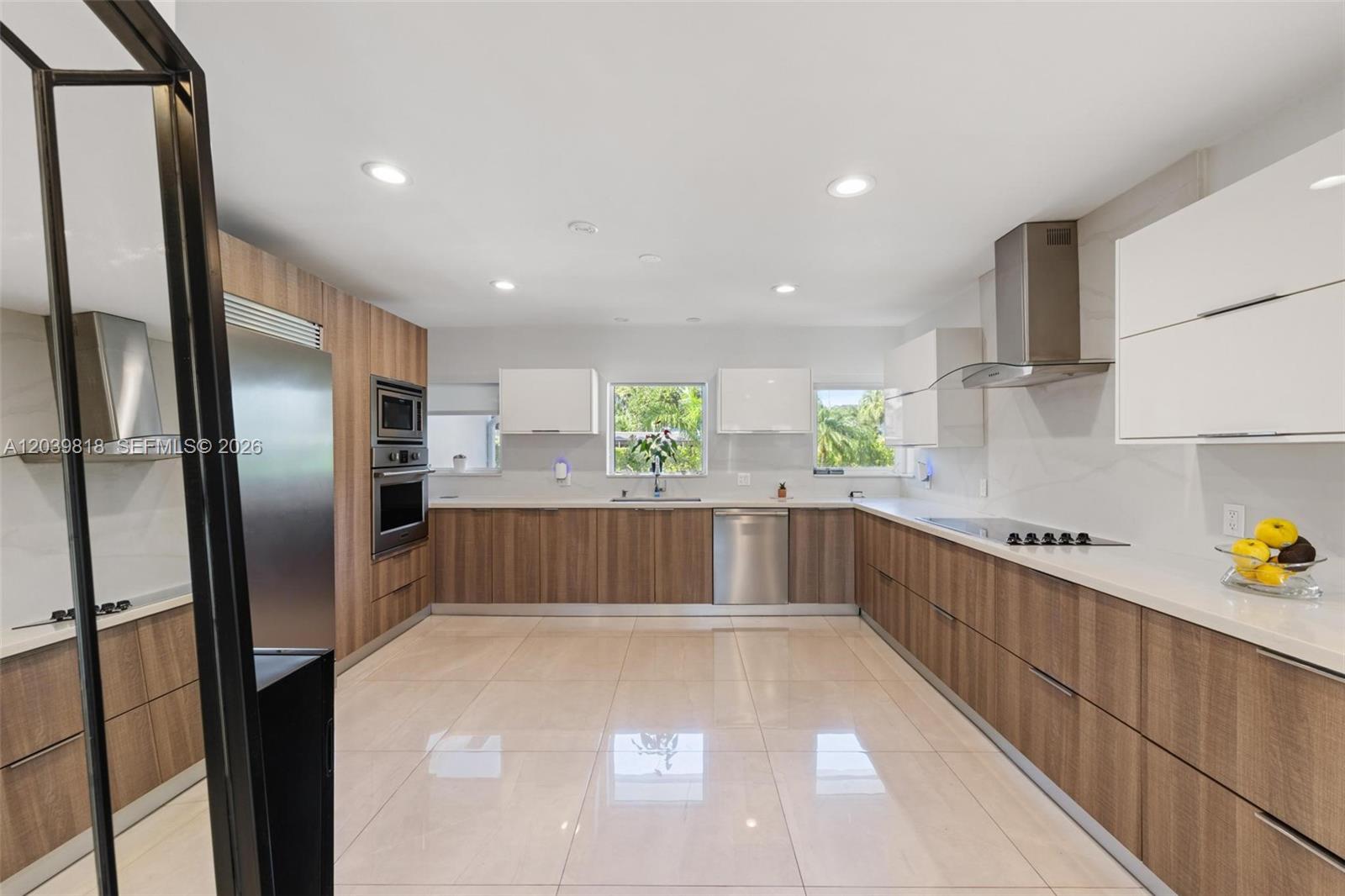 A modern kitchen features wood-grain lower cabinets, white upper cabinets, and light tile flooring — 1014 Jefferson St, Hollywood FL 33019, HOLLYWOOD, FL