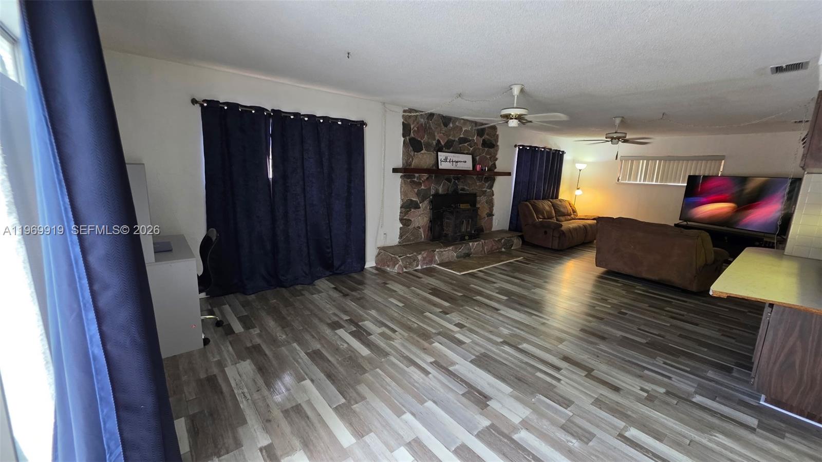 A living room features a stone fireplace, wood-look flooring, and a large television — 18227 BRANCH ROAD, Hudson FL 34667, HUDSON, FL