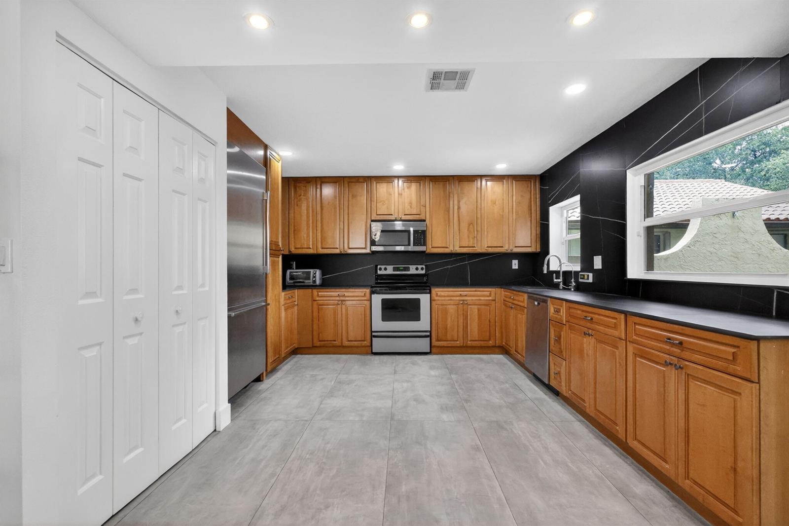 A kitchen features wood cabinets, stainless steel appliances, black countertops, and gray tile flooring — 1230 NW 22nd Avenue, Delray Beach FL 33445, DELRAY BEACH, FL
