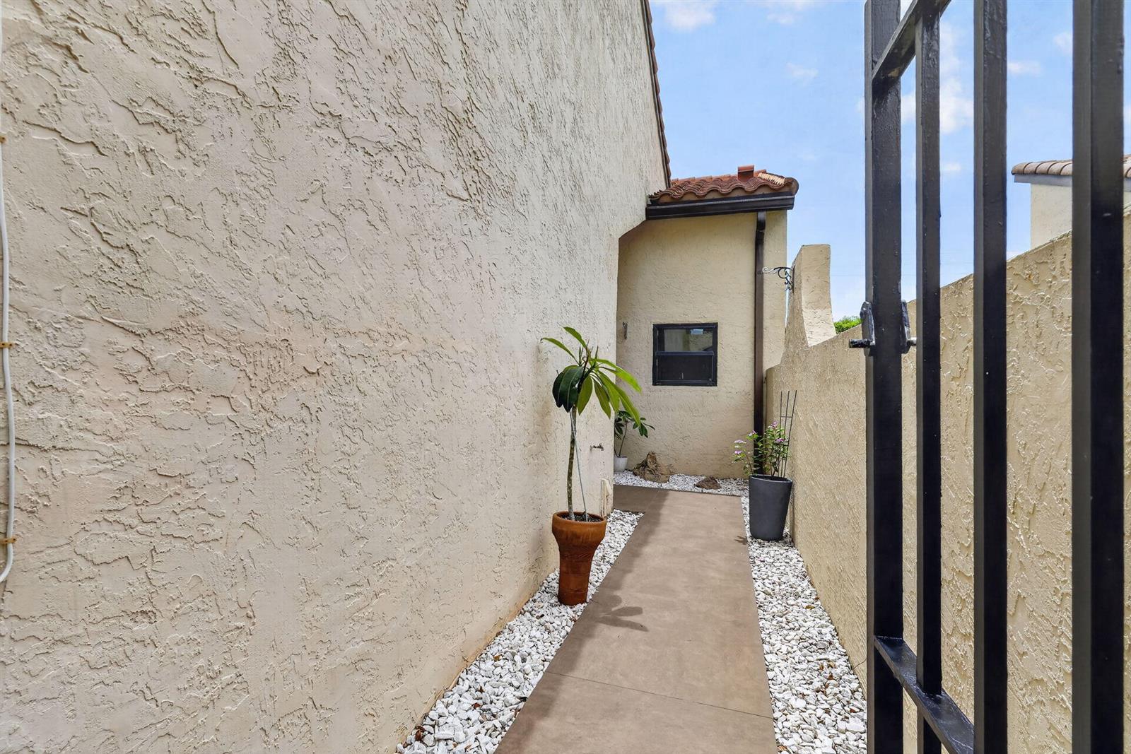 A narrow concrete walkway leads between a stucco house wall and a perimeter wall — 1230 NW 22nd Avenue, Delray Beach FL 33445, DELRAY BEACH, FL